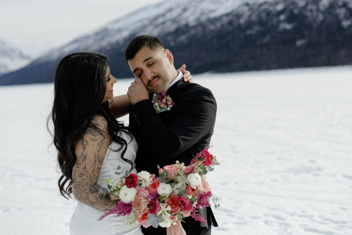 Bride and groom eloping in late winter in Alaska on a frozen lake with mountains all around them. 