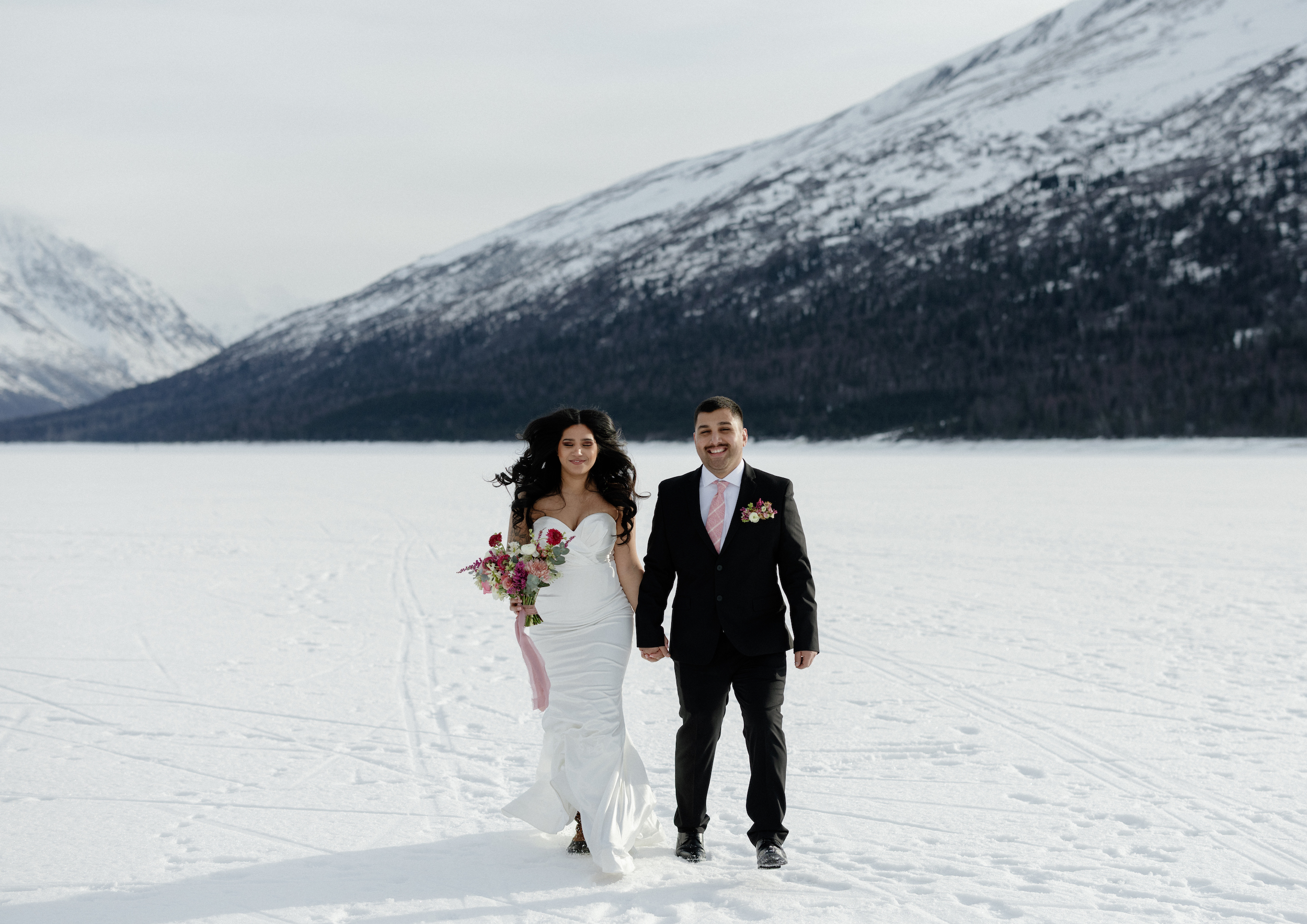Couple holding hands with Alaskan mountains in the background during their destination wedding.
