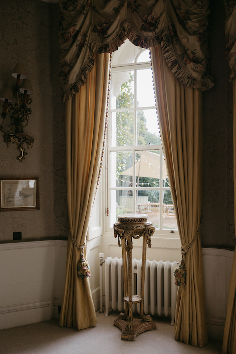 A window with yellow curtains and a pedestal set beside inside the venue.