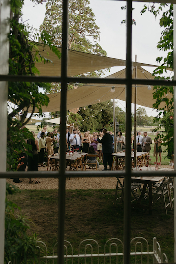 A group of people gathered under a tent listening to speeches during a welcome party at Pylewell Park.